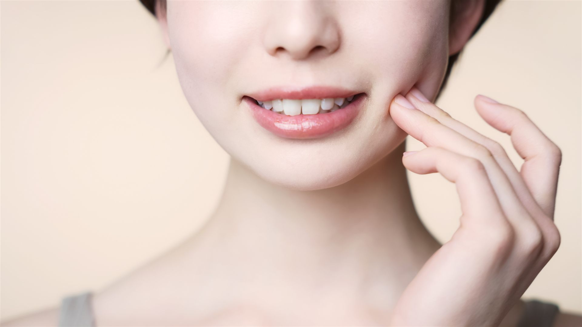 頬に手を添えて微笑む女性の、自然な白い歯の口元